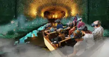 Un grupo de personas con cascos de realidad virtual se sientan en un barco a la deriva a través de un túnel oscuro y brumoso, rodeados de figuras fantasmales que brillan y de un inquietante paisaje subterráneo.